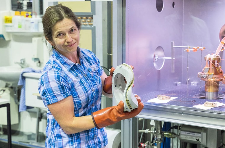 Gruppenleiterin Dr. Eve Stenson mit der Modellform einer nicht planaren Magnetspule. Unten können mit Hilfe eines Führungsschlitzes supraleitende Bänder aufgewickelt werden, die im Teststand (im Hintergrund) überprüft werden.