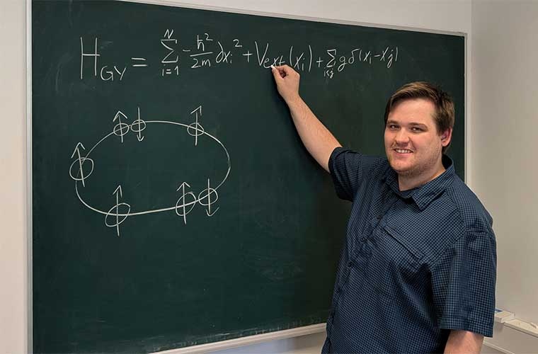 Timothy George Backert vor einer Tafel mit einer schematischen Darstellung des untersuchten Systems, also der Atome auf einem Ring.