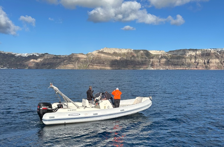 Drei Personen auf einem motorgetriebenen Schlauchboot, eine Frau schaut durch ein Fernglas, eine Person beugt sich über den Rand des Bootes ins Wasser