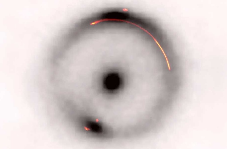 Überlagerung der Infrarotemission (schwarz-weiß) mit der Radioemission (farbig). Das dunkle Objekt mit geringer Masse befindet sich in der Lücke im hellen Teil des Bogens auf der rechten Seite.