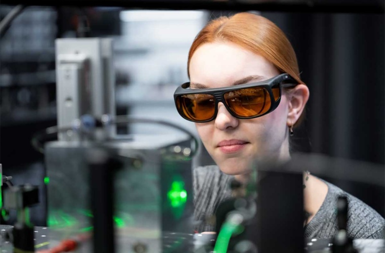 Mit einer Schutzbrille wirft Stöllner einen Blick in die Versuchskammer (im Vordergrund), wo zwei Laserstrahlen ein einzelnes Teilchen einfangen.