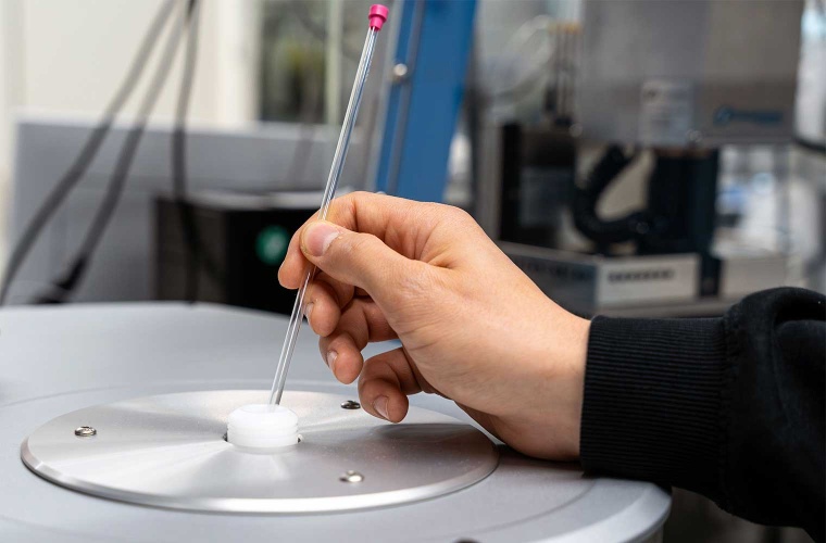 Eine chemische Probe in einem Glasröhrchen wird in ein NMR-Spektrometer geführt
