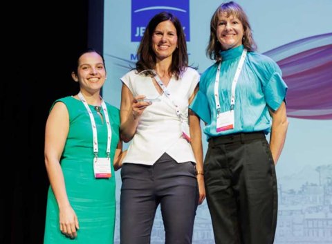 Elizabeth Illy von HÜBNER Photonics und Estefania Cervantes von Edmund Optics, die Co-Vorsitzenden der EPIC-Arbeitsgruppe für Nachhaltigkeit, überreichen den EPIC Sustainability Award 2026 an Katrin Fleischer, Managerin Investor Relations & Sustainability bei Jenoptik