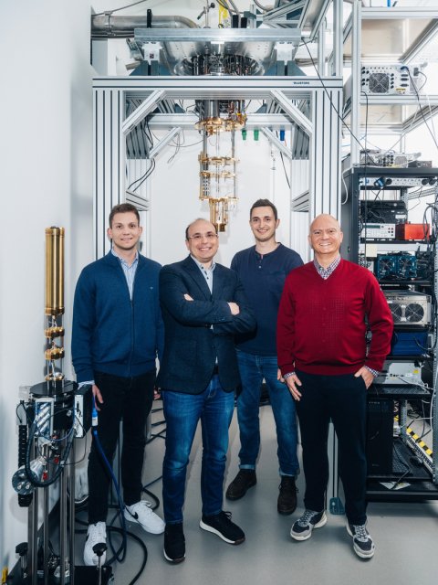 Von rechts nach links stehen Rostyslav Serha, Andrii Chumak, David Schmoll und Sebastian Knauer vor einem Kryostaten. Dieses Gerät dient zur Erzeugung und Stabilisierung extrem niedriger Temperaturen, wodurch die kontrollierte Anregung und präzise Detektion von Magnonen ermöglicht wird.